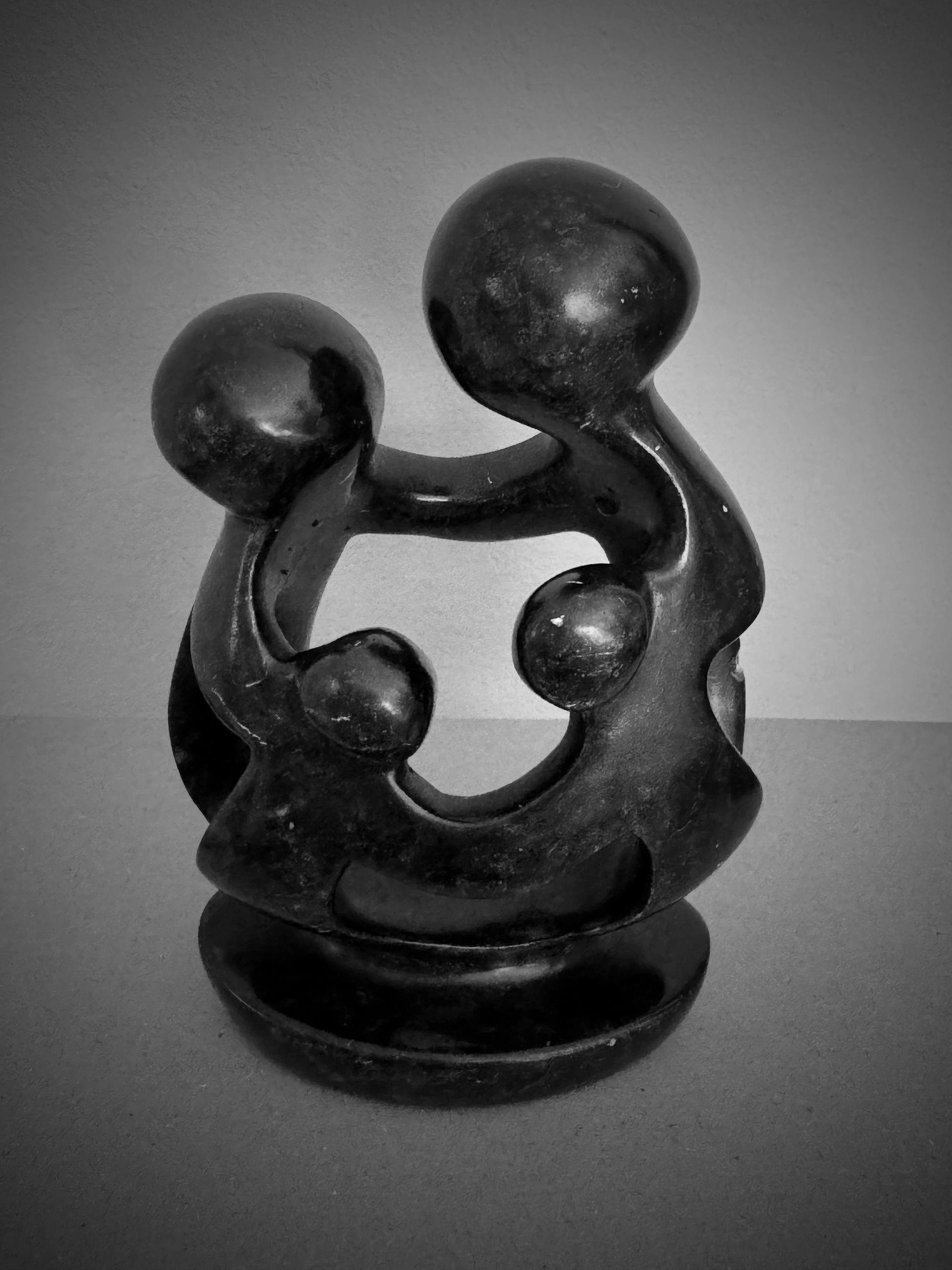 Dark stone sculpture of abstract adult and child figures gathered together.